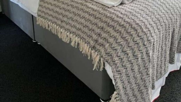 A neatly made bed with a grey and white zigzag patterned blanket, a grey headboard, and a framed picture on the wall.