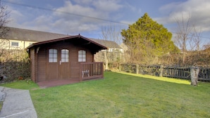 Une cabane en bois avec un porche, une petite terrasse et une cour gazonnée.
