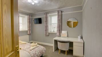A bedroom with a bed, a desk, a chair, a television, and a window with curtains.