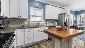 A modern kitchen with white cabinets, a granite countertop, a stainless steel refrigerator, and a wooden island. - 4 bedroom 3 bath home in Cherry Grove. Screened porch Firepit. 2 blocks to ocean (North Myrtle Beach)