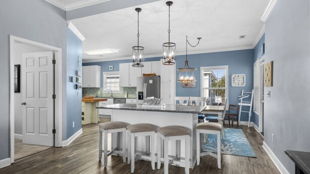 A modern kitchen with a central island, bar stools, pendant lighting, and a view of the dining area. - 4 bedroom 3 bath home in Cherry Grove. Screened porch Firepit. 2 blocks to ocean (North Myrtle Beach)