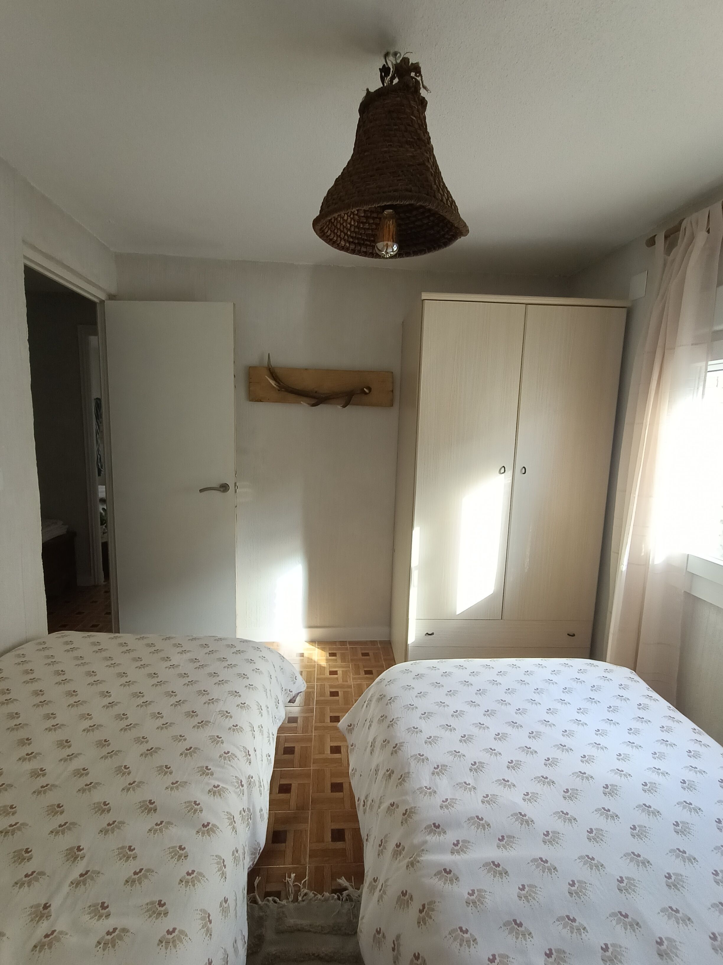 Un dormitorio con dos camas, un armario de madera, una lámpara colgante y una puerta que da a otra habitación.