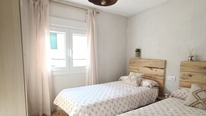 Ein Schlafzimmer mit zwei Betten, einem Holzkopfende, einer Pendelleuchte und einem Fenster mit Vorhängen.