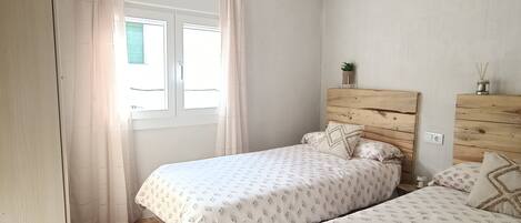 Een slaapkamer met twee bedden, een houten hoofdbord, een hanglamp en een raam met gordijnen.