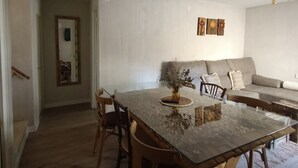 Ein Essbereich mit einem Glastisch, Holzsesseln und einer Couch im Hintergrund.