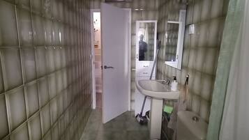 A bathroom with a toilet, sink, and mirror. The walls are tiled, and there is a door leading to another room.