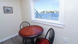 Un coin repas avec une table et deux chaises, une fenêtre donnant sur un plan d’eau et un quai, et un tableau encadré accroché au mur.