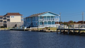 Une propriété située au bord de l’eau, avec une grande maison bleue dotée d’un balcon et d’un escalier menant à l’entrée.