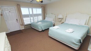 A hotel room with two beds, a window with a view, a door, and a ceiling fan. - Egret Escape 2 Queen Deluxe Fin N Feather (Nags Head)