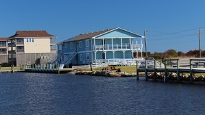 Een pand aan het water met een groot, blauw huis, voorzien van een balkon en een trap naar de ingang.