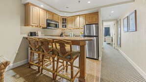 A modern kitchen with wooden cabinets, a stainless steel refrigerator, and a bar area with wicker chairs.