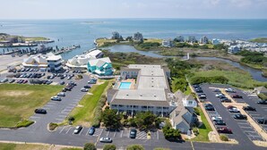 An aerial view of a coastal hotel with a parking lot, a swimming pool, and a view of the sea.