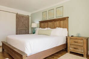 Quarto com cama de madeira, mesa de cabeceira, abajur e porta deslizante.