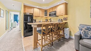 Una cocina compacta con armarios de madera, un refrigerador negro, un microondas y una pequeña isla con taburetes de bar.