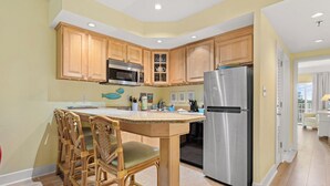A kitchen with wooden cabinets, a stainless steel refrigerator, and a central island with chairs.