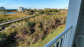Un balcón con vistas a la costa, incluyendo un paseo marítimo de madera y edificios a lo lejos.
