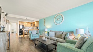 A living room with a sofa, coffee table, and a dining area with a kitchen in the background. - Relaxing Ocean Wynnes at Villas of Hatteras Landing - 1 Bedroom Near-Beach Condos with Pool Access! (Hatteras)