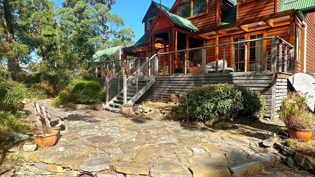 A wooden cabin with a stone patio, surrounded by trees.