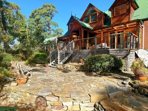 Une cabane en bois avec un patio en pierre, entourée d’arbres.