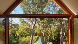A triangular window with a view of a forested area and a building with a green roof.