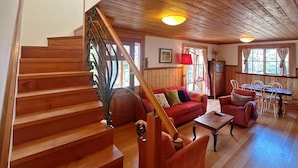 A wooden staircase leading to a living area with a red sofa, a dining table, and a chandelier.
