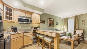 A kitchen with wooden cabinets, a microwave, a sink, and a dining area with a table and chairs.