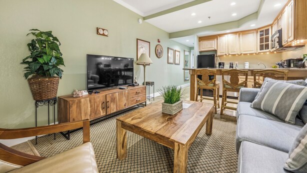 Una sala de estar con televisor, muebles de madera, un comedor con sillas y una cocina con armarios.