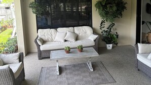 A living room with a white sofa, two potted plants, a coffee table, and a ceiling fan. - Beautiful & Peaceful Room in Ooralea – Private Queen Room (Ooralea)