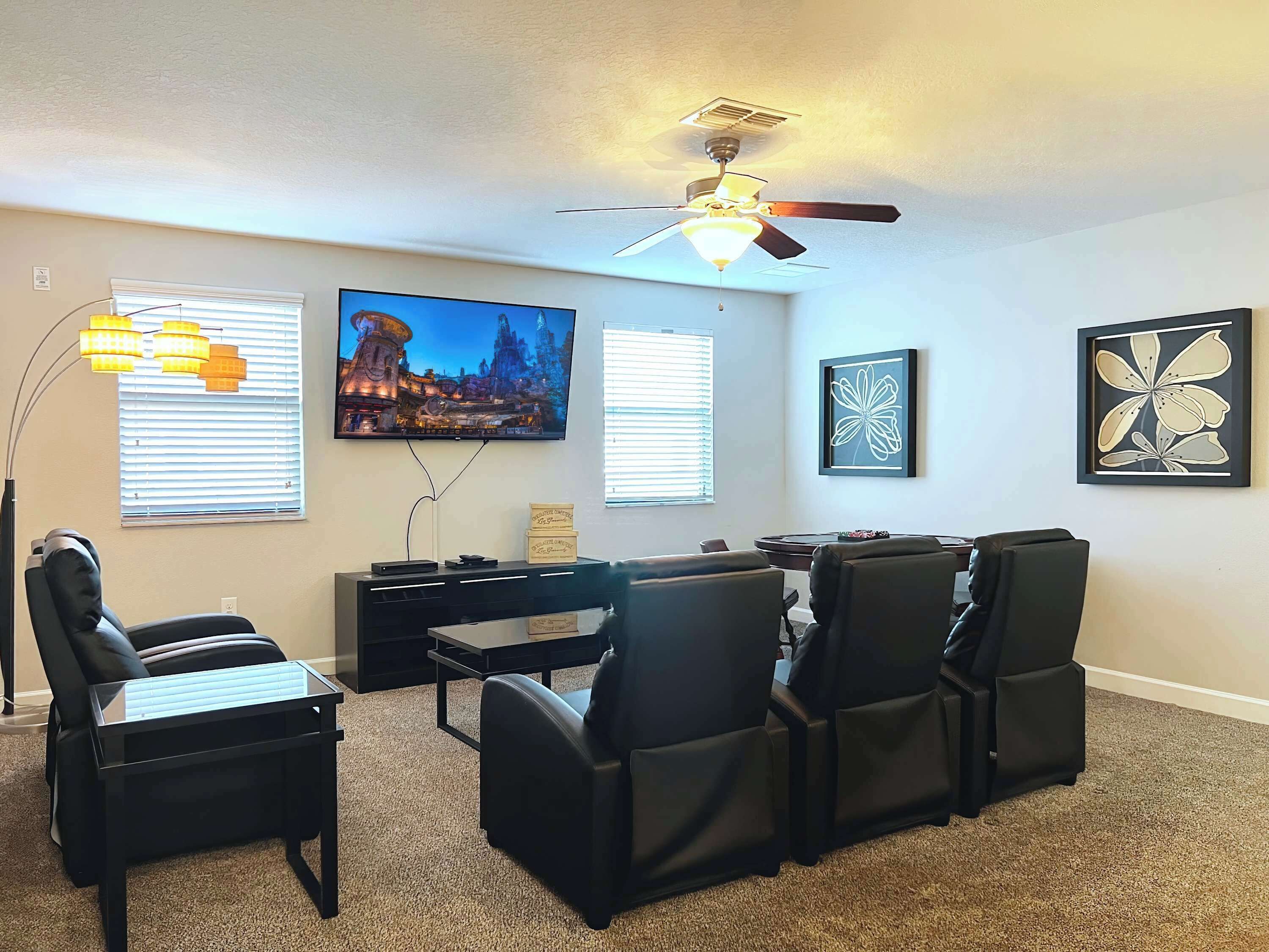 A living room with a ceiling fan, a flat-screen TV, a coffee table, and four chairs.