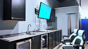 Een moderne keuken met een inbouwoven, een spoelbak en een aanrecht. Er hangt een televisie aan de muur en er staat een stoel in de hoek.