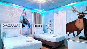 Habitación de hotel con dos camas, una mesita de noche, una lámpara y una pared con personajes animados.