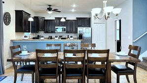 Una cocina moderna con armarios oscuros, una isla central y un comedor con seis sillas de madera y una mesa.