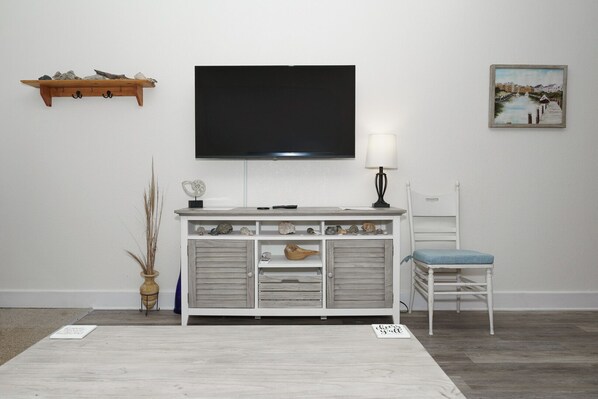 A room with a white cabinet, a television, a chair, and a painting on the wall. - Toes In The Water at Villas of Hatteras Landing - 1 Bedroom Near-Beach Condos with Pool Access! (Hatteras)