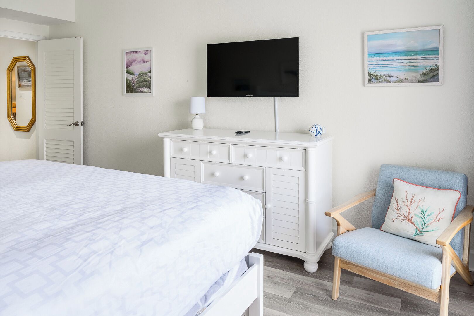 Un dormitorio con una cama, un aparador, una silla, un televisor y dos cuadros en la pared.