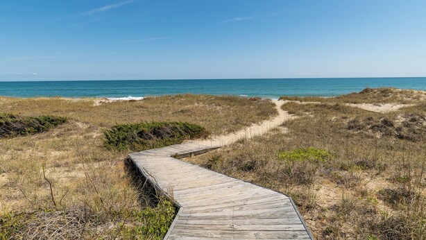 A wooden boardwalk leading to a beach with clear skies.