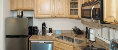 A kitchen with wooden cabinets, stainless steel appliances, a granite countertop, and a dish rack.