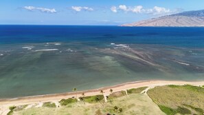 Una vista aerea di una zona costiera con acque limpide, una spiaggia sabbiosa e un paesaggio collinare sullo sfondo.