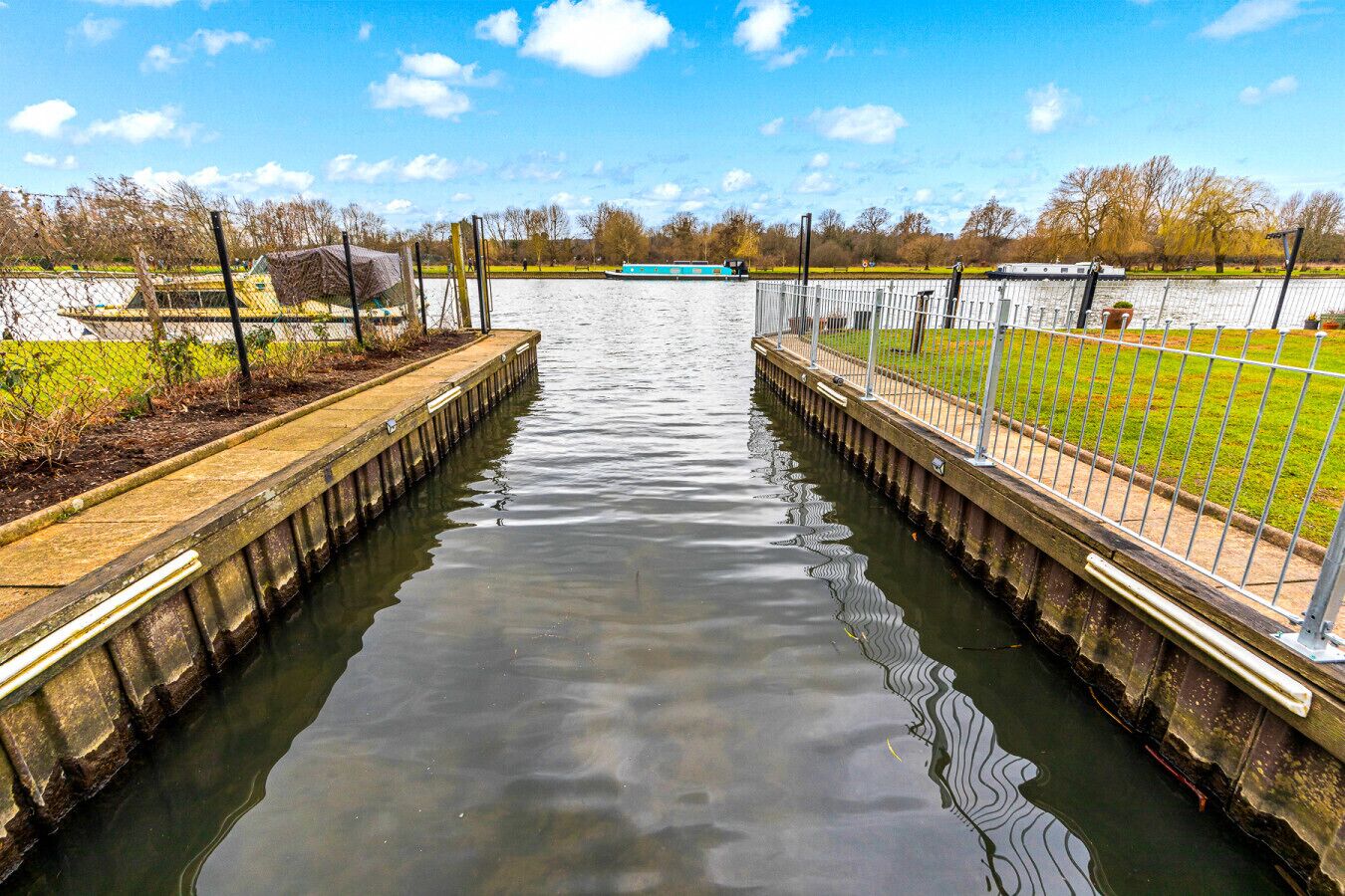 A canal with a boat docked on the right side, surrounded by a fence and grassy areas.