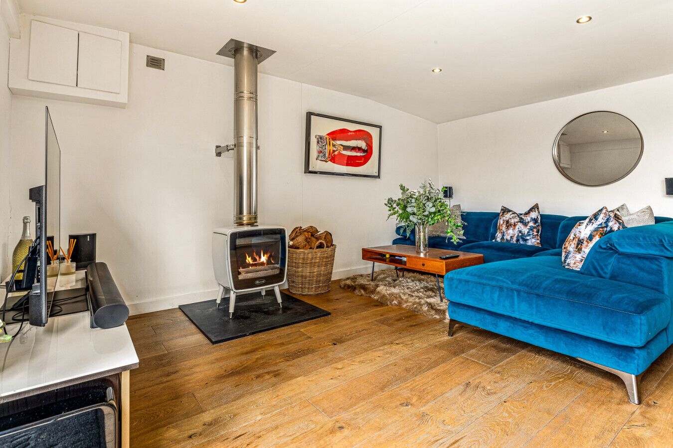 Ein Wohnzimmer mit Kaminofen, einem blauen Sofa, einem Spiegel und einem gerahmten Kunstwerk an der Wand.