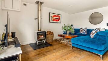 Ein Wohnzimmer mit Kaminofen, einem blauen Sofa, einem Spiegel und einem gerahmten Kunstwerk an der Wand.