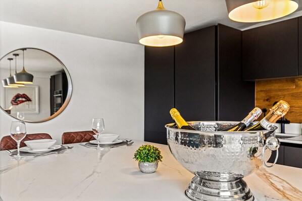 A modern dining area with a marble table, a large silver bowl with champagne bottles, a small potted plant, and a mirror on the wall.
