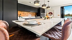 A modern kitchen with a large island, pendant lighting, and leather seating.