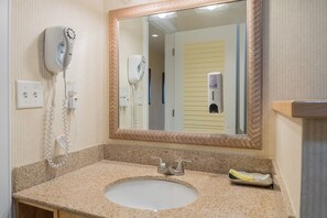 A bathroom with a granite countertop sink, a mirror with a decorative frame, a hairdryer, and a hand dryer.