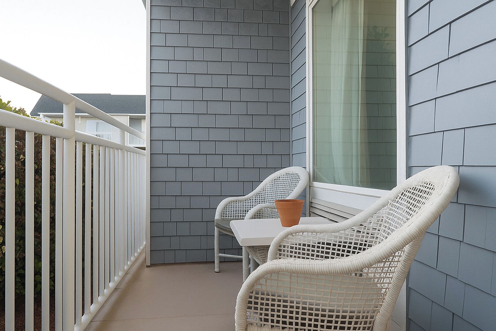 A balcony with two wicker chairs, a table, and a potted plant.