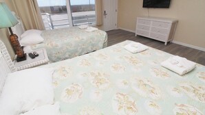 Habitación de hotel con dos camas, un televisor, un aparador blanco y vistas al exterior.