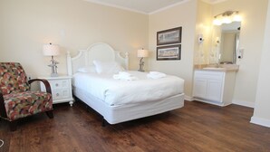 Une chambre d’hôtel comprenant un lit, une chaise, une table de chevet, une lampe, un miroir et une coiffeuse avec un lavabo.