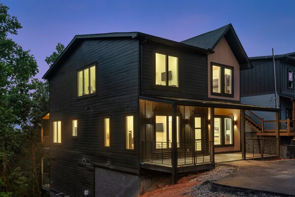 A modern two-story house with a covered porch, large windows, and a staircase leading to the upper level.