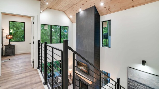 Ein modernes Interieur mit Holzboden, einer Treppe mit schwarzen Geländern und großen Fenstern mit Blick auf viel Grün.