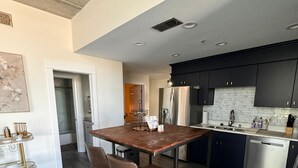 A modern kitchen with dark cabinets, a stainless steel refrigerator, and a wooden dining table with two chairs.