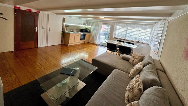 A spacious living area with a sofa, a glass coffee table, and a kitchen in the background. - 2-room apartment in prime city center location with terrace & DreiWelten-Card (Bad Dürrheim)